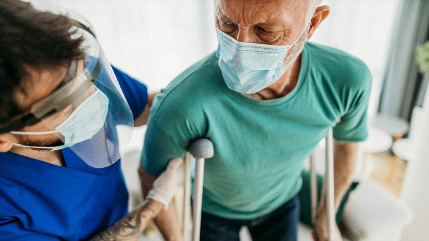 Closeup of man on crutches being helped to walk by a physical therapist