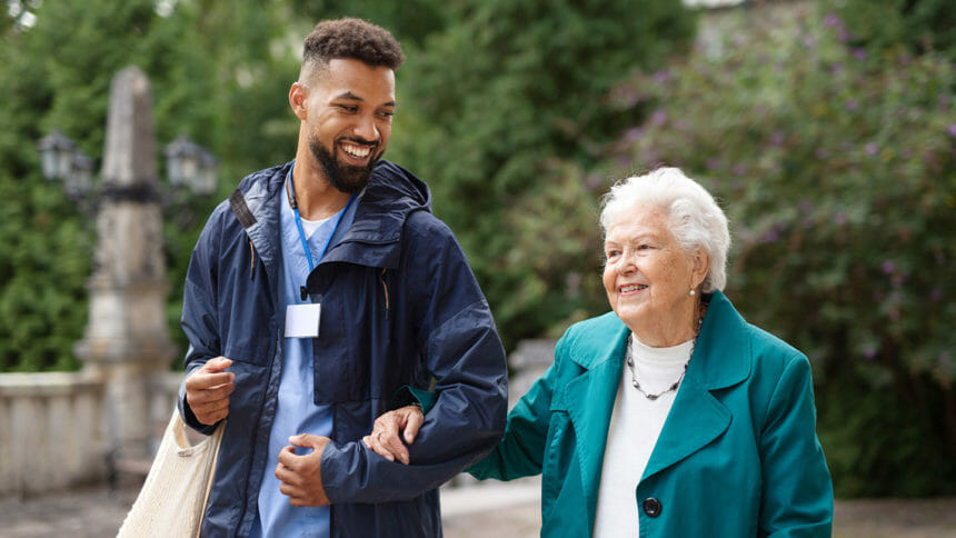 Senior woman and caregiver outdoors on a walk in park, talking.