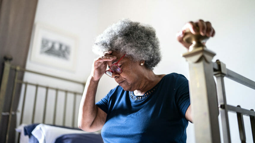 Senior woman with headache sitting in the bed at home